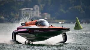 Hydroplane racing boat skimming water surface at high speed with spray and shoreline backdrop